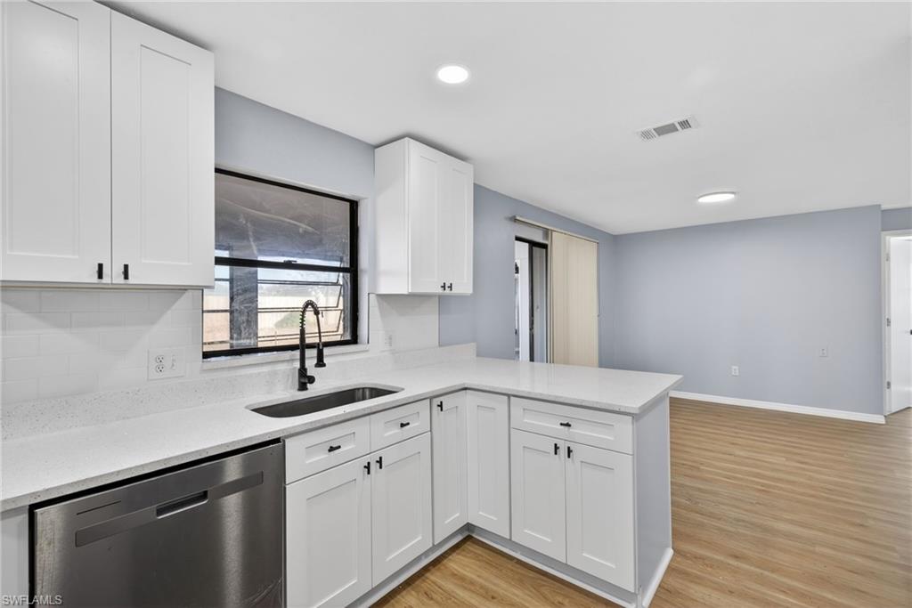 Kitchen with stainless steel dishwasher, light wood-style flooring, white cabinetry, light stone counters, and recessed lighting