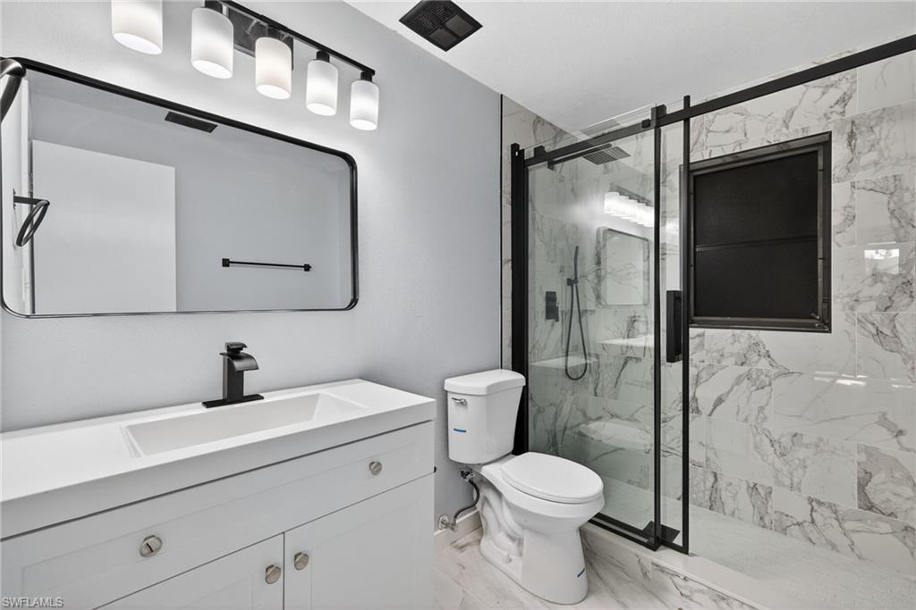 Bathroom featuring vanity, a marble finish shower, and light marble finish floors