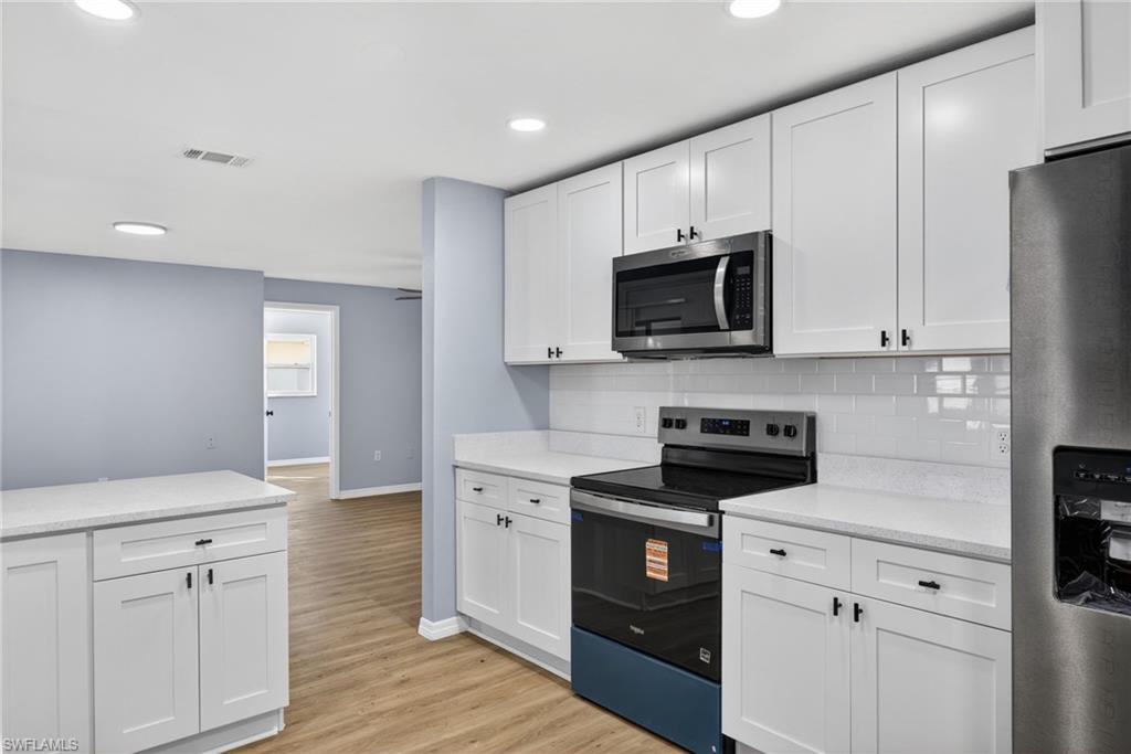 Kitchen with stainless steel appliances, white cabinetry, light wood-style floors, tasteful backsplash, and recessed lighting