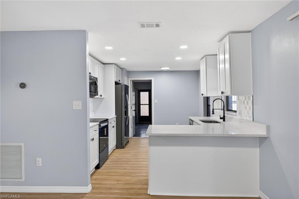 Kitchen featuring white cabinetry, a peninsula, electric range, light stone counters, and stainless steel fridge