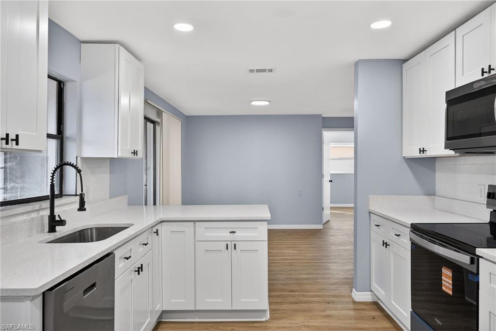 Kitchen with stainless steel appliances, a peninsula, white cabinets, light wood-style flooring, and light stone countertops