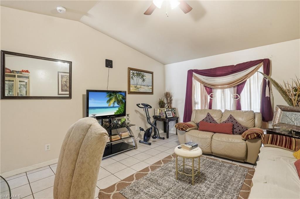 Living room with ceiling fan, light tile patterned floors, and lofted ceiling
