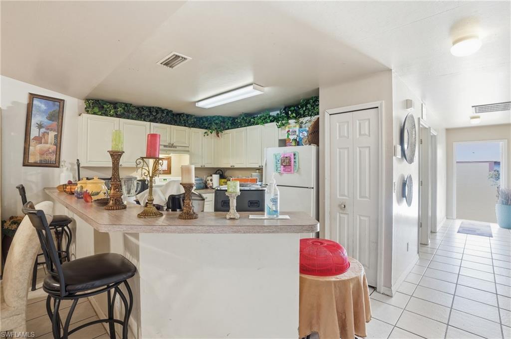 Kitchen featuring a kitchen bar, white cabinetry, light tile patterned floors, freestanding refrigerator, and light countertops