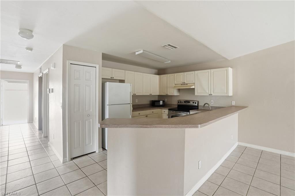 Kitchen with electric stove, light tile patterned floors, a peninsula, and freestanding refrigerator