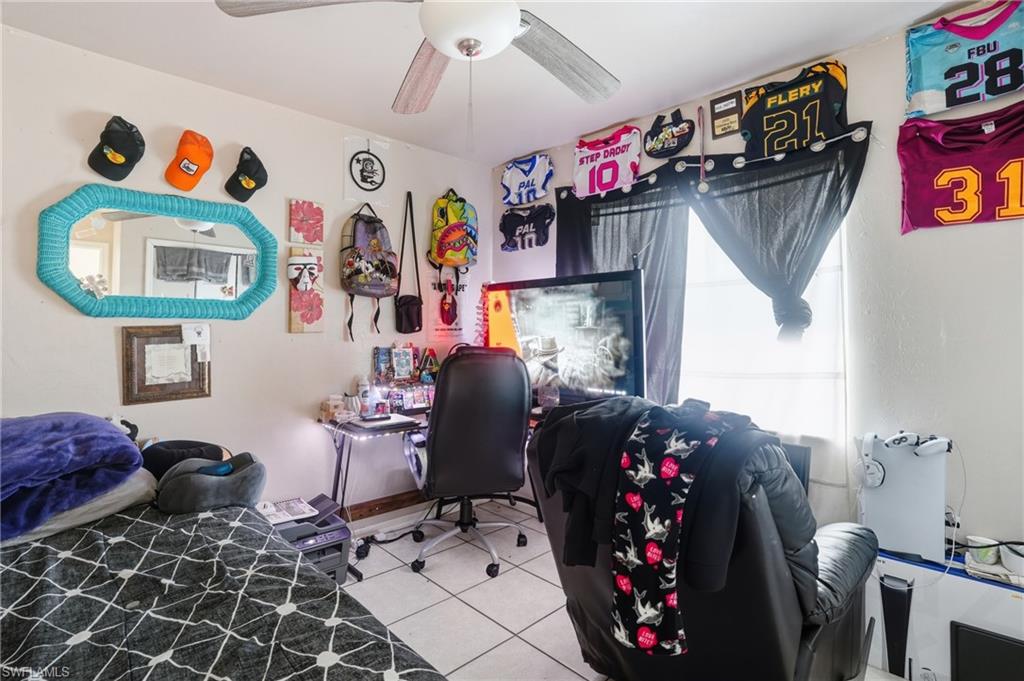 Bedroom with an office area, light tile patterned flooring, and ceiling fan