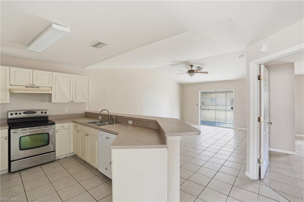 Kitchen with electric stove, a peninsula, ceiling fan, light tile patterned flooring, and vaulted ceiling