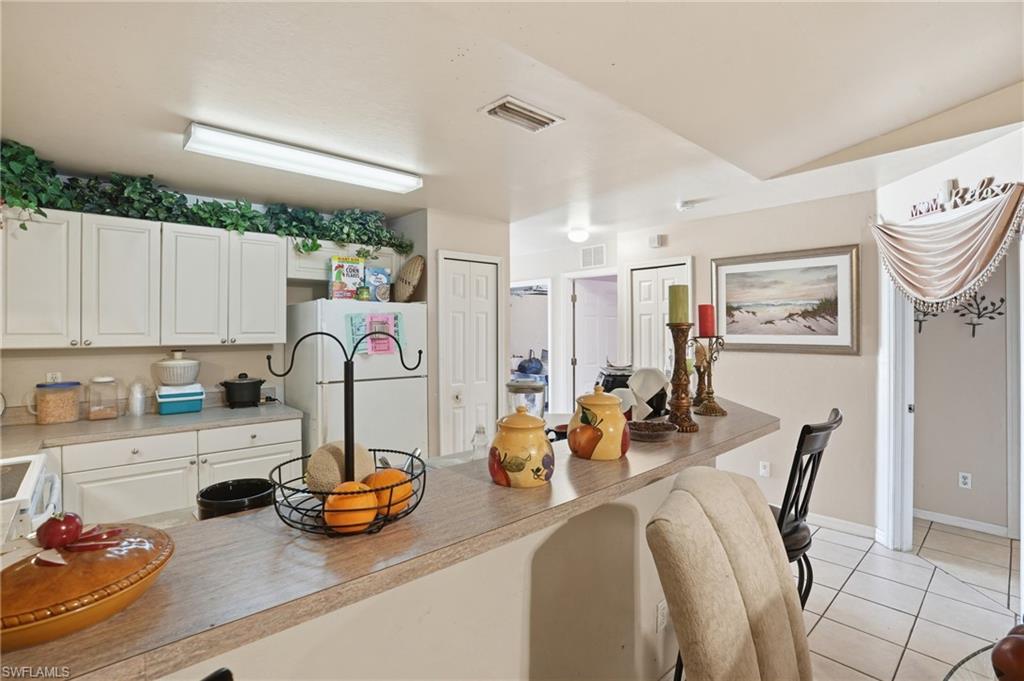 Kitchen with freestanding refrigerator, white cabinetry, light tile patterned floors, light countertops, and a kitchen bar