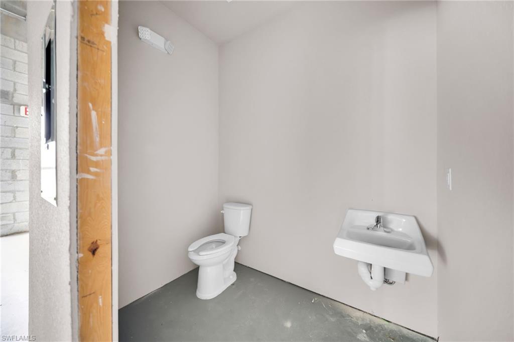 Restroom featuring a white toilet, wall-mounted sink with chrome faucet, and light gray painted walls