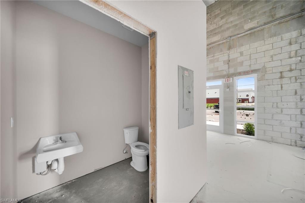 Rough-in bathroom with wall-mounted sink and toilet, positioned adjacent to an open area with white-painted concrete block walls and multiple large windows