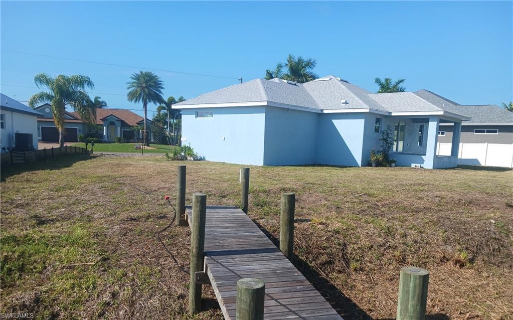 Waterfront property featuring a private wooden dock, a blue-painted exterior, a light gray shingle roof, and a covered patio area