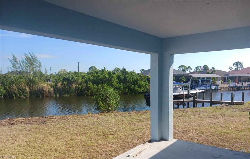 Covered patio featuring a concrete slab and painted stucco columns, overlooking a canal with a natural shoreline and a wooden dock