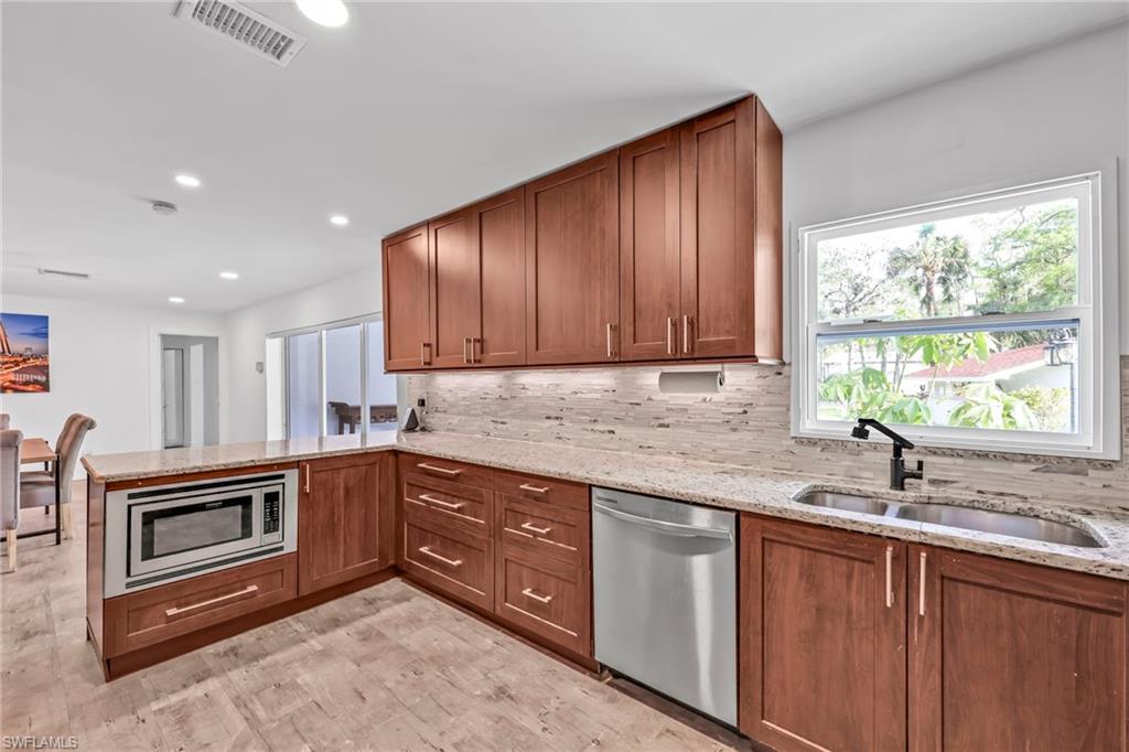 Kitchen with light stone countertops, stainless steel appliances, wood finish cabinets, tasteful backsplash, and a peninsula
