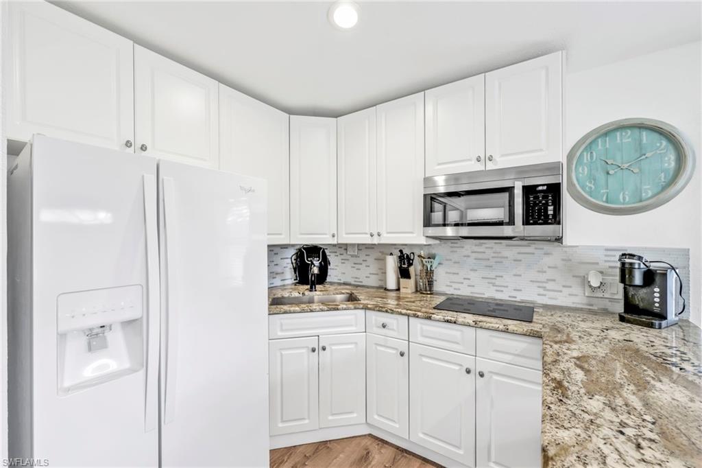 Kitchen with white fridge with ice dispenser, light stone countertops, white cabinetry, stainless steel microwave, and light wood finished floors