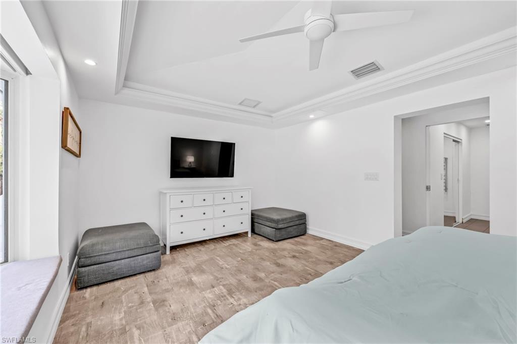 Bedroom featuring light wood-style flooring, recessed lighting, a ceiling fan, ornamental molding, and a tray ceiling