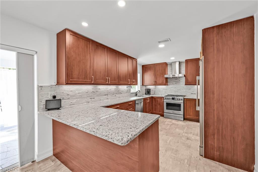 Kitchen with wood finish cabinets, a peninsula, stainless steel appliances, light stone countertops, and recessed lighting