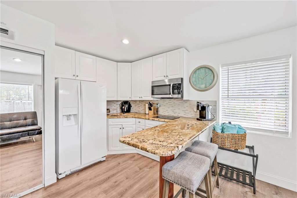 Kitchen featuring light stone countertops, white refrigerator with ice dispenser, white cabinetry, light wood finished floors, and a kitchen bar