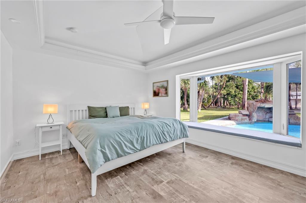 Bedroom featuring light wood-style floors, a tray ceiling, and ceiling fan