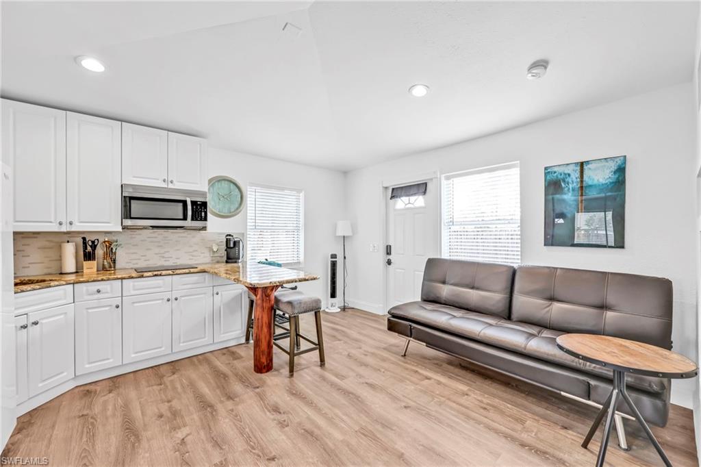 Kitchen featuring a breakfast bar, light stone countertops, light wood-style flooring, white cabinets, and stainless steel microwave