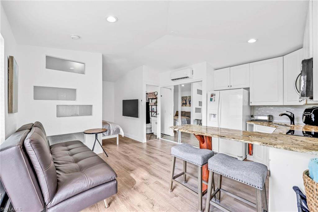 Kitchen with a breakfast bar area, light stone countertops, a peninsula, white fridge with ice dispenser, and light wood-type flooring
