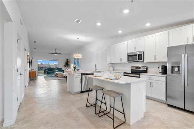 Kitchen featuring stainless steel appliances, pendant lighting, a center island, white cabinetry, and kitchen peninsula