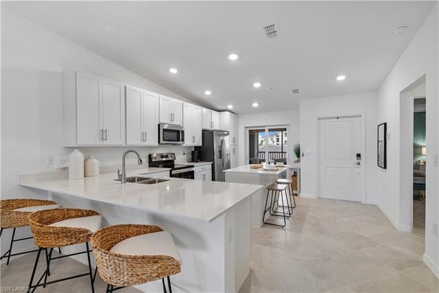 Kitchen featuring kitchen peninsula, sink, appliances with stainless steel finishes, white cabinets, and a kitchen breakfast bar