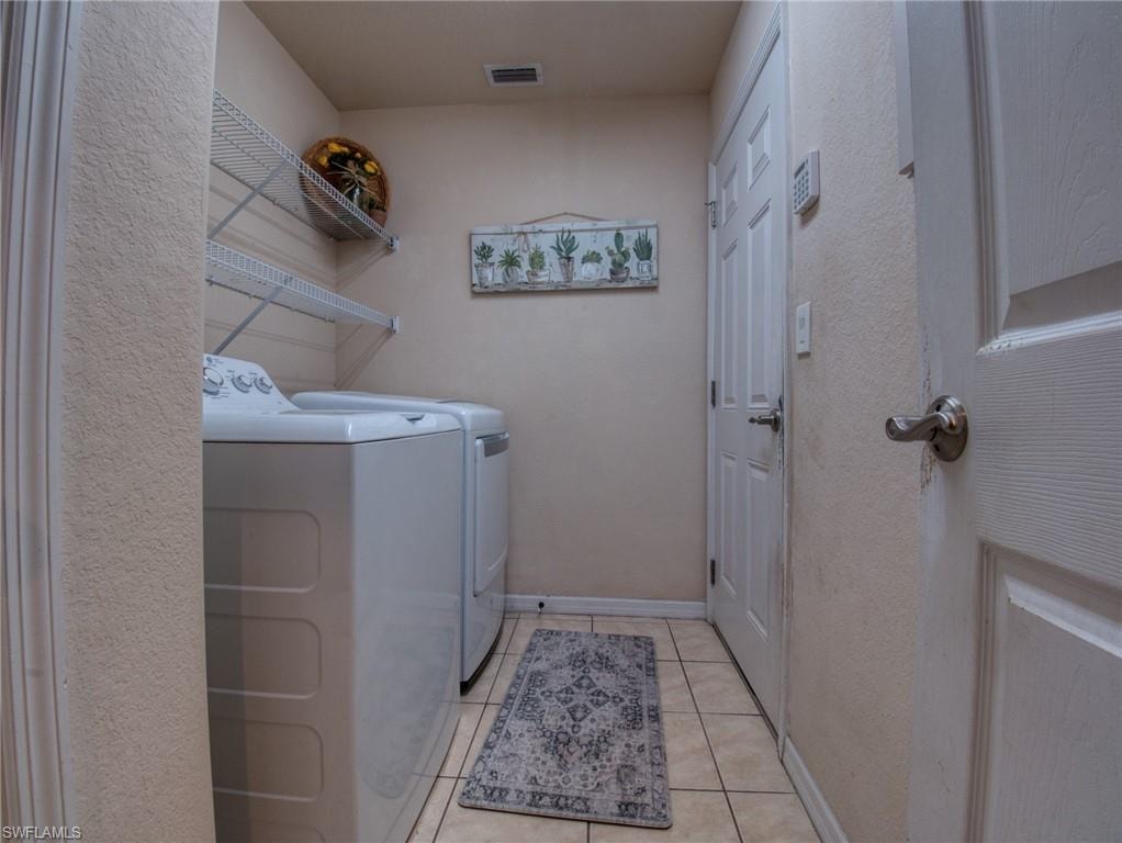 Laundry room featuring washer and clothes dryer, light tile patterned floors, and a textured wall