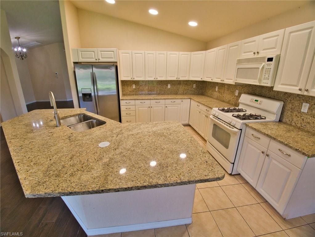Kitchen featuring a large central island with a double basin sink and a high-arc faucet, granite countertops, white cabinetry with silver hardware, a gas range, and tile flooring