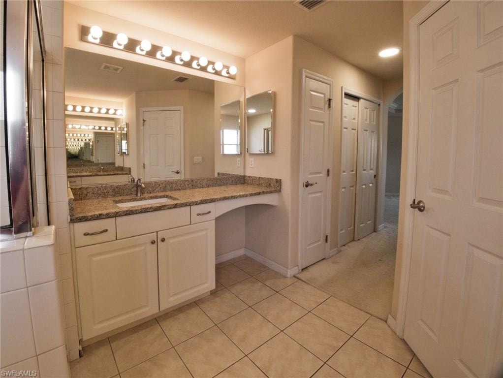 Bathroom vanity featuring a speckled countertop, integrated sink, and full-width mirror with overhead lighting