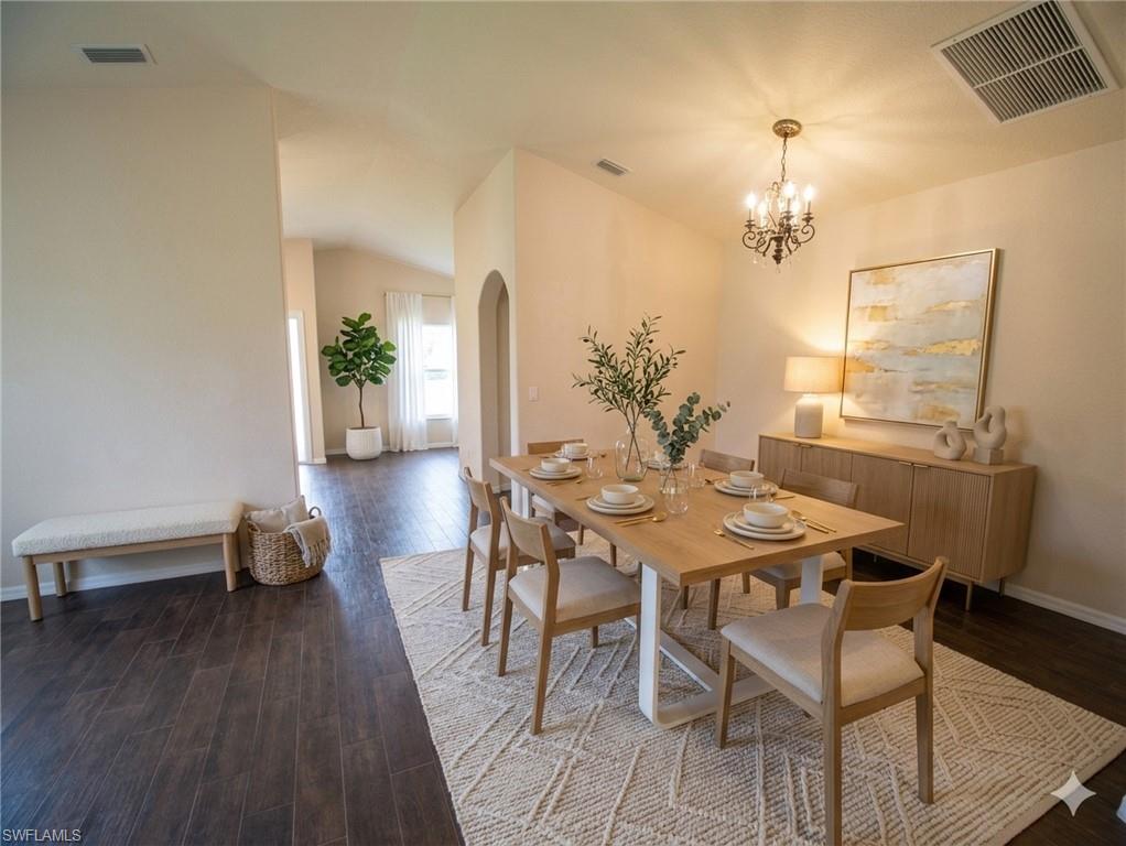 Dining area featuring vaulted ceilings, dark wood-finish flooring, an arched doorway, and a brass chandelier