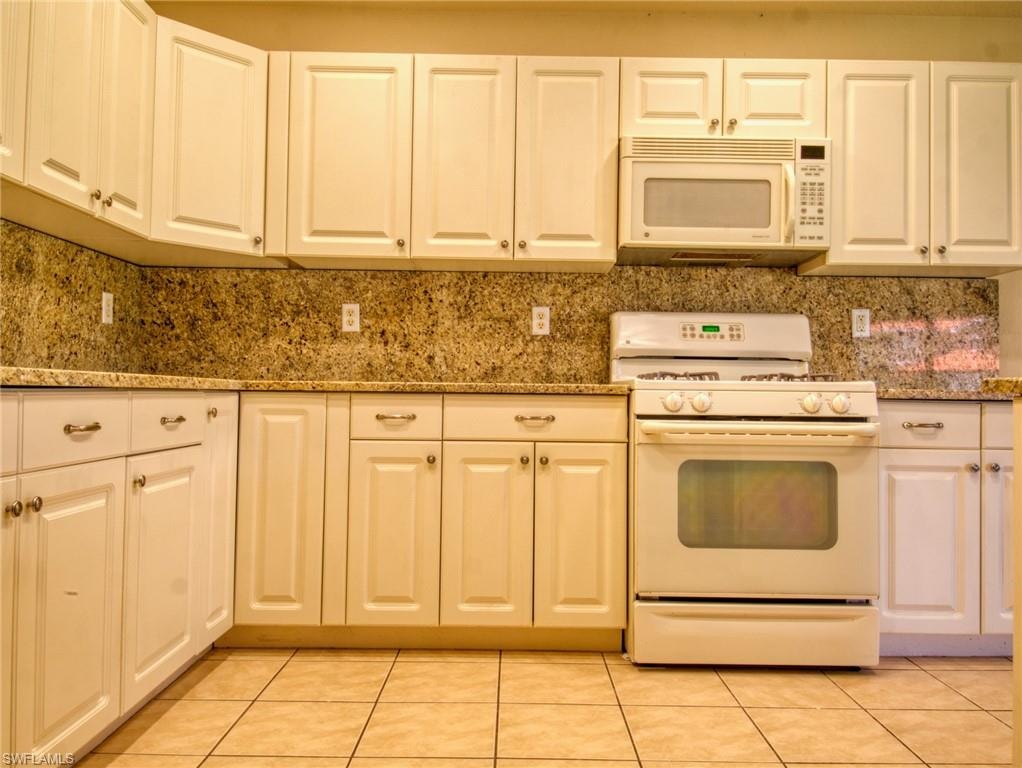 Kitchen featuring white cabinetry, stone countertops, integrated microwave, and a white oven/range