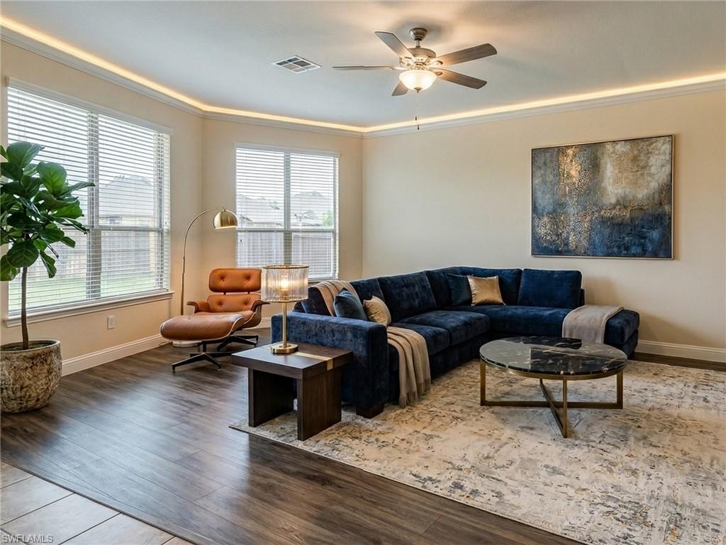 Living area featuring wood-finish flooring, a ceiling fan with integrated lighting, and crown molding with accent lighting