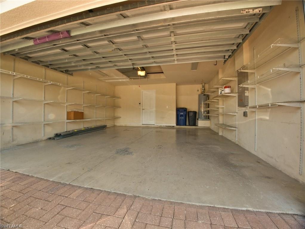 Spacious garage featuring extensive built-in shelving, a smooth concrete floor, and brick paver driveway entry