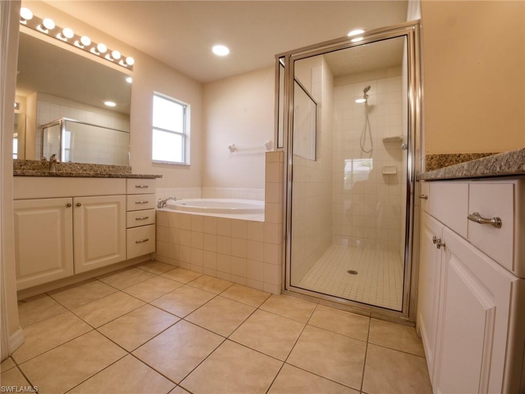 Bathroom featuring a tiled floor, dual vanities with granite countertops, a built-in soaking tub, and a separate glass-enclosed shower
