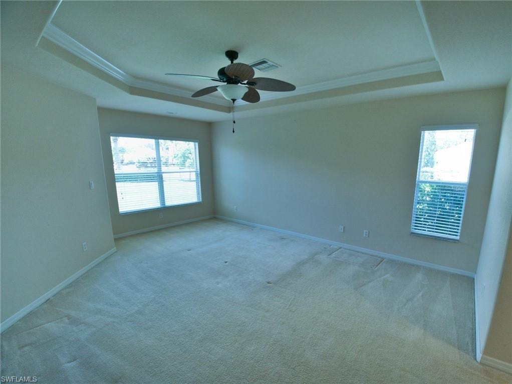 Spacious room featuring a tray ceiling with crown molding, a ceiling fan, and carpeted flooring