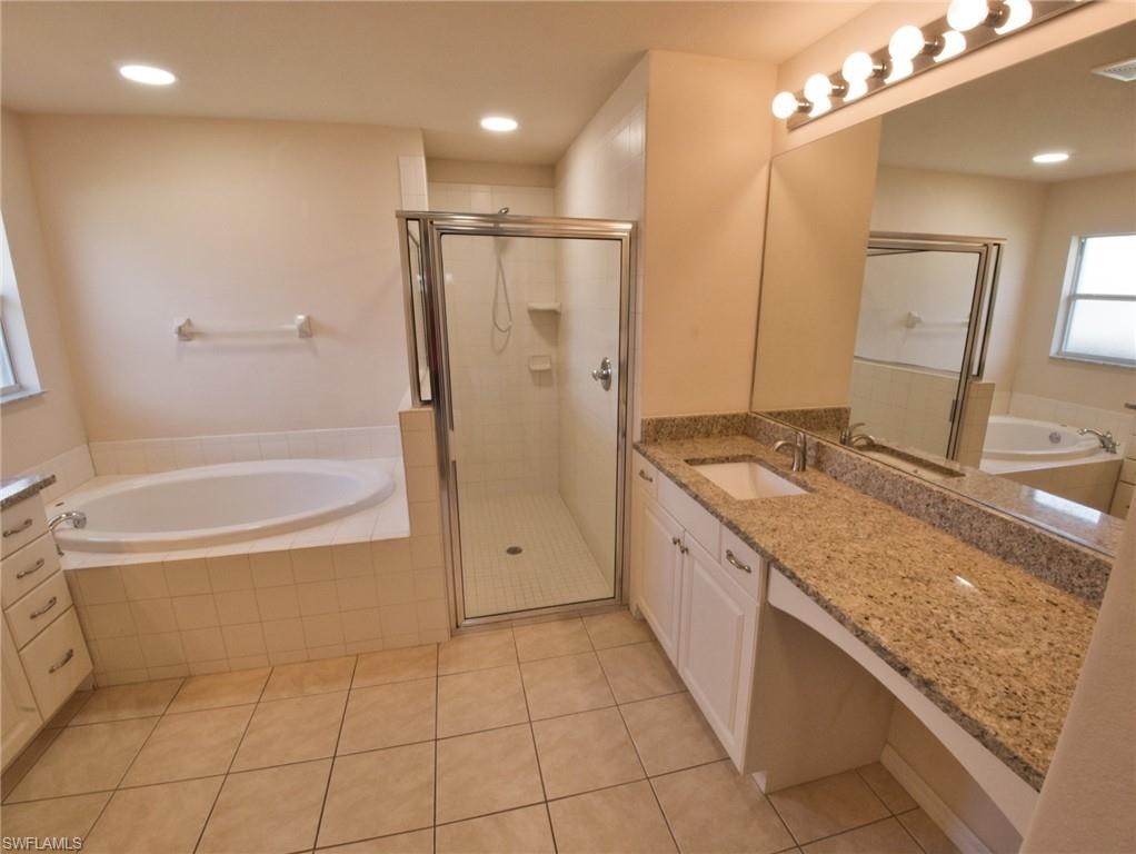 Bathroom featuring a tiled floor, a built-in soaking tub with tiled surround, a glass-enclosed shower, a vanity with a white basin sink, and a granite-finish countertop