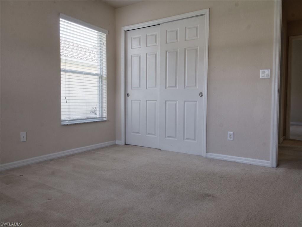 Bedroom featuring neutral-toned carpeting, a window with horizontal blinds, and a closet with white bi-fold doors