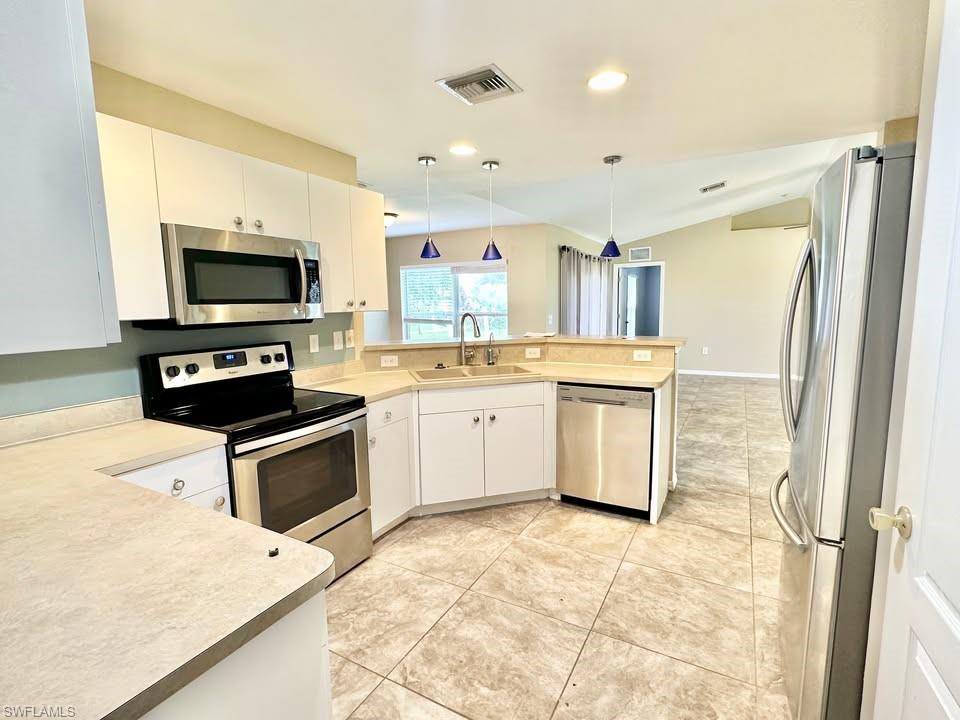 Kitchen with stainless steel appliances, a peninsula, light countertops, white cabinetry, and lofted ceiling