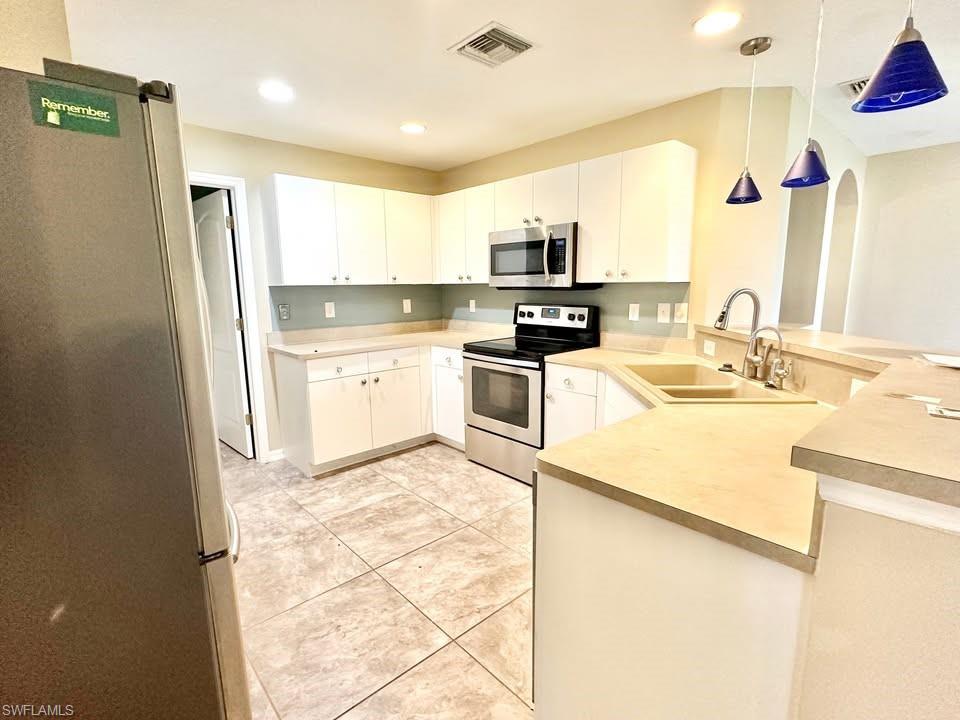 Kitchen with stainless steel appliances, a peninsula, arched walkways, light countertops, and decorative light fixtures