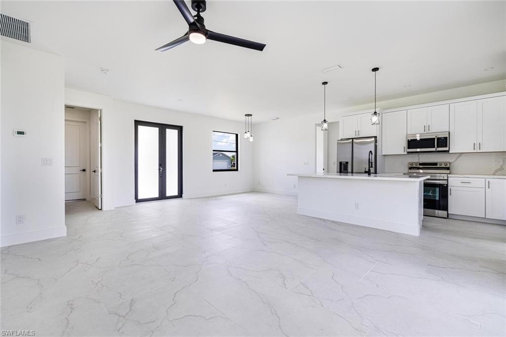 Contemporary kitchen featuring a large center island with integrated sink, white cabinetry, stainless steel appliances, and geometric pendant lighting