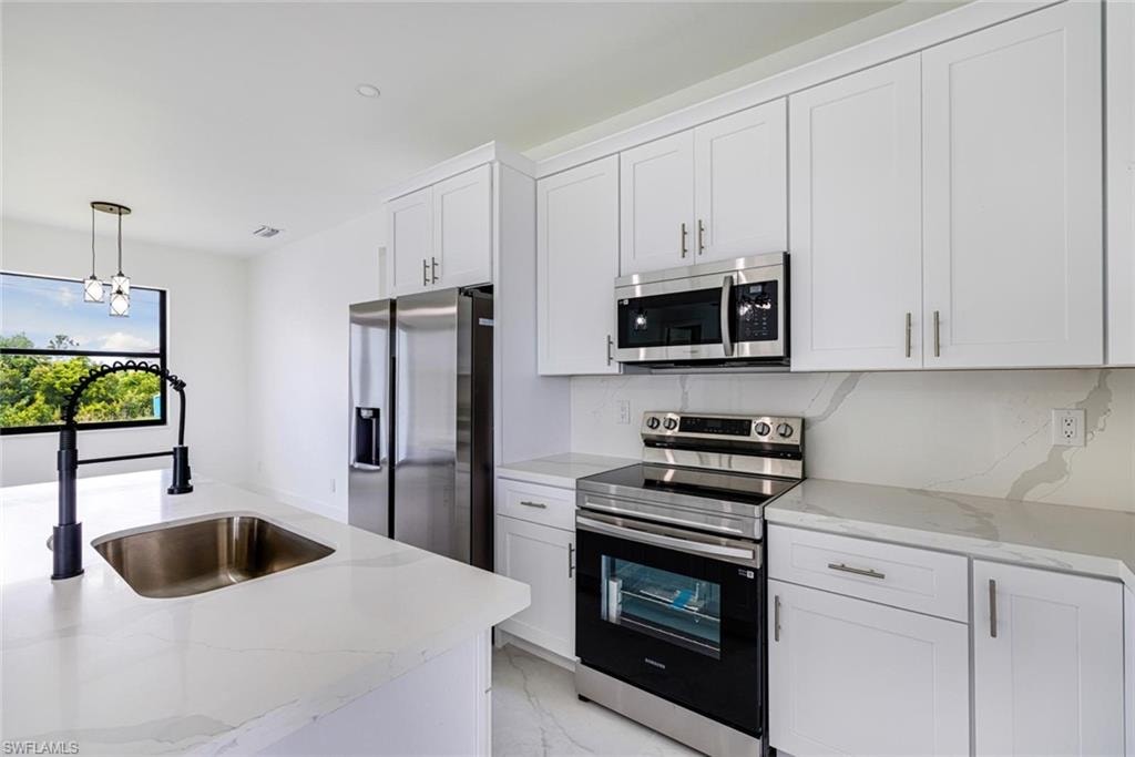 Open-concept living and kitchen featuring white cabinetry with stainless steel appliances, a large island with seating for multiple, and pendant lighting