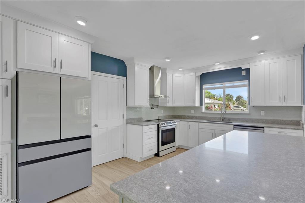 Kitchen featuring stainless steel appliances, white cabinetry, light wood-style floors, light stone countertops, and recessed lighting