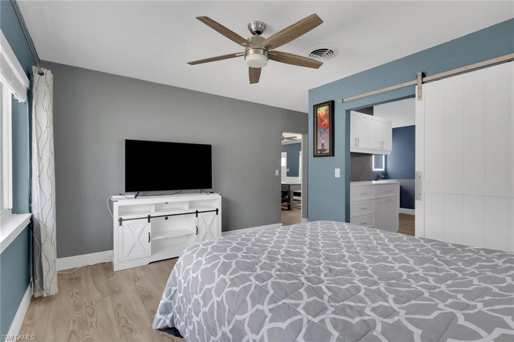 Bedroom with a barn door, light wood finished floors, and ceiling fan