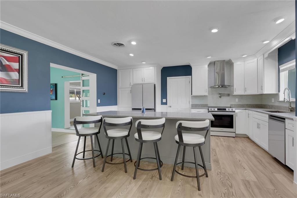 Kitchen featuring electric range oven, a center island, white cabinetry, light wood-style floors, and ornamental molding