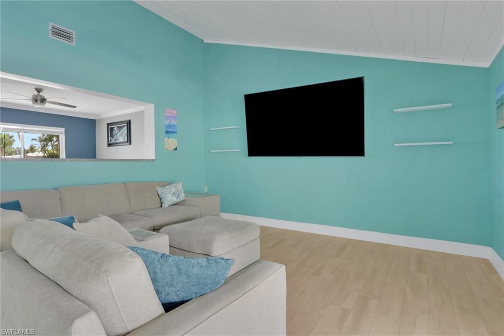 Living room with wood finished floors, lofted ceiling, ceiling fan, and ornamental molding