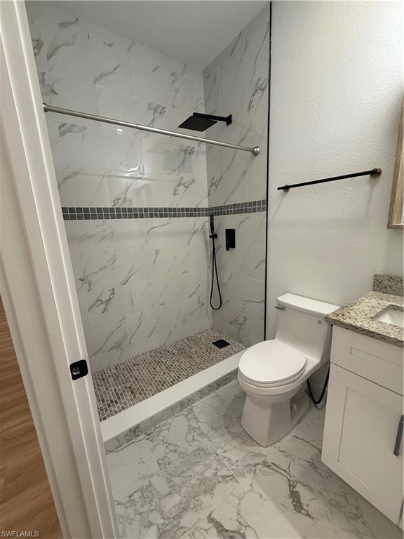 Full bath with vanity, a marble finish shower, a textured wall, and light marble finish flooring