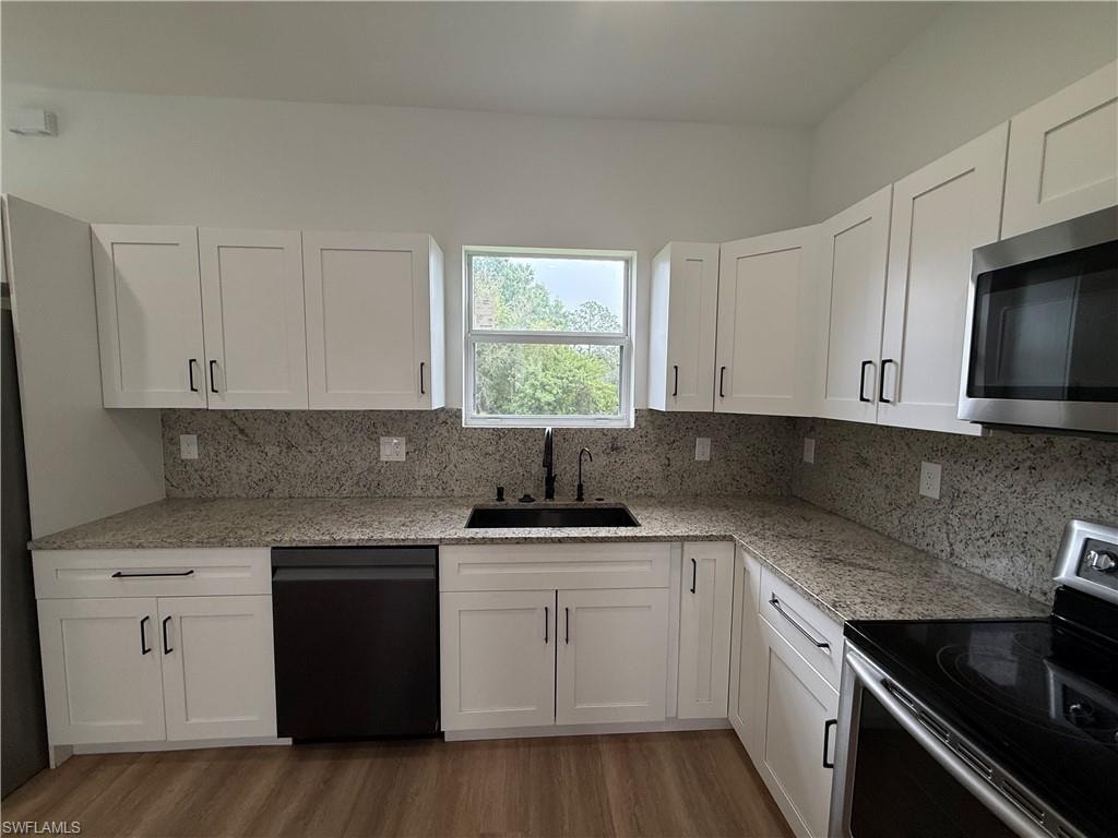 Kitchen featuring stainless steel appliances, light stone counters, white cabinetry, and light wood finished floors