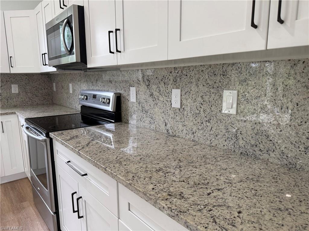 Kitchen featuring stainless steel appliances, white cabinets, backsplash, light stone countertops, and light wood finished floors