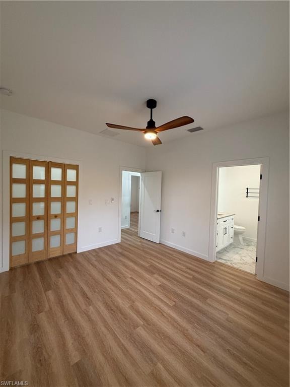 Unfurnished bedroom with ceiling fan, ensuite bathroom, and light wood-style flooring