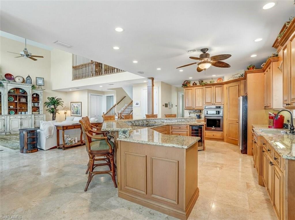 Kitchen featuring a ceiling fan, a breakfast bar area, light stone countertops, open floor plan, and wine cooler - Virtually Edited Image
