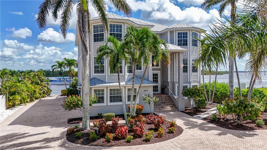 View of front of house featuring a water view, a standing seam roof, curved driveway, and stucco siding - Virtually Edited Image